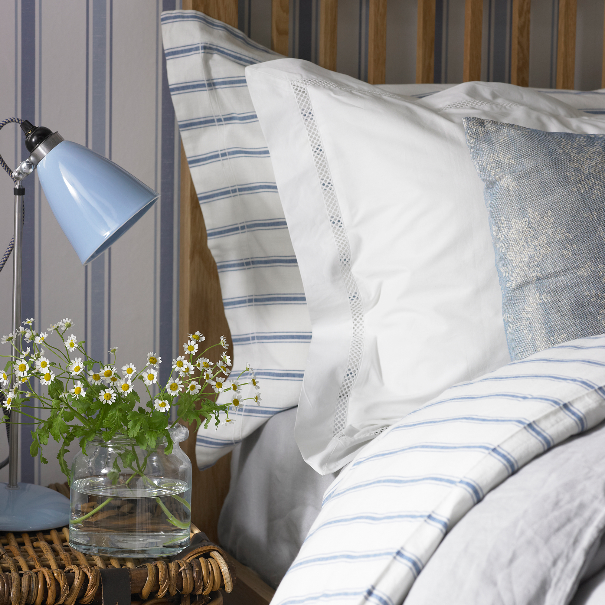 Bed with pillows, blue and white striped bedding and flowers on nightstand