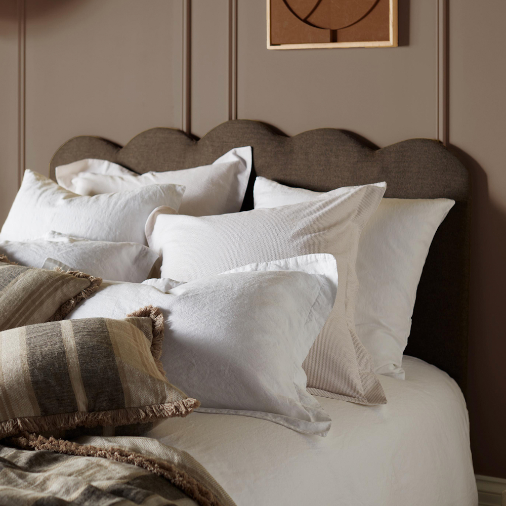 Six white pillows against a brown headboard with smaller striped brown pillow at the front
