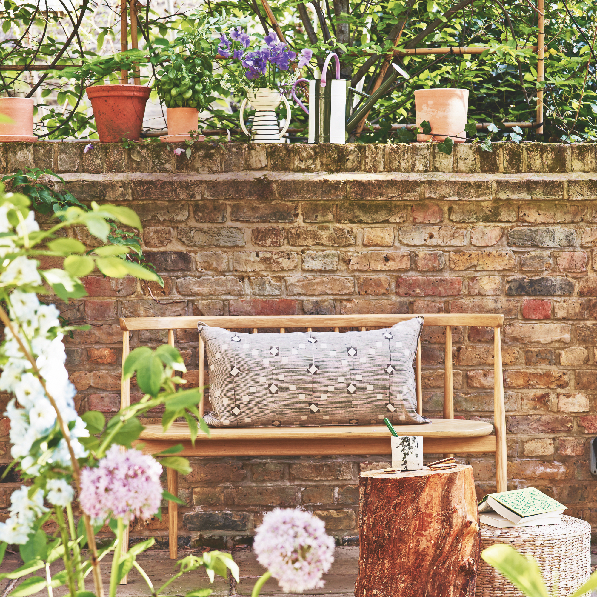 mid century modern style bench with retro print cushion against garden wall, pots and planters on the wall above, wooden trunk coffee table