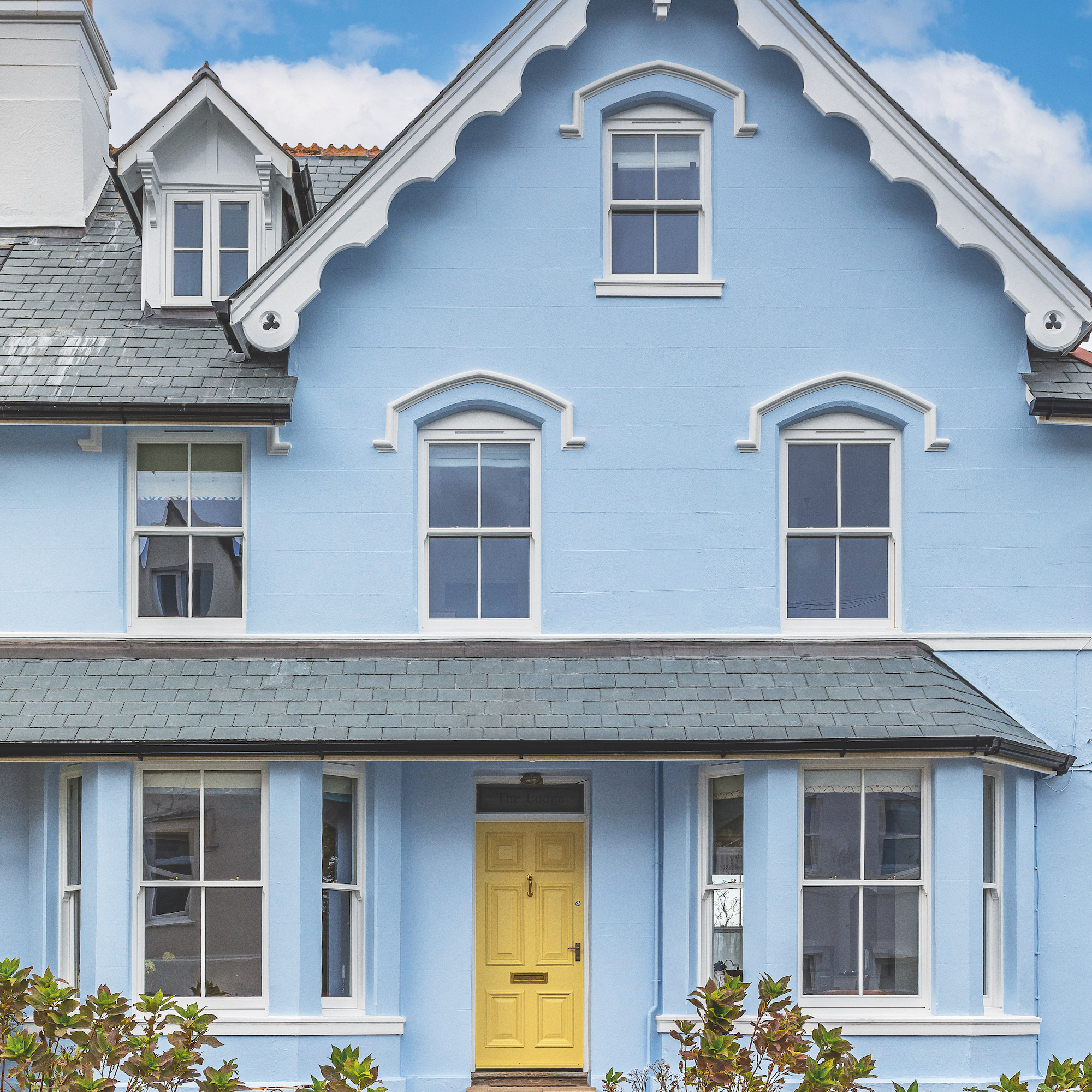 Victorian house with pitched roof and white gables, pale blue painted render and yellow front door, with porch