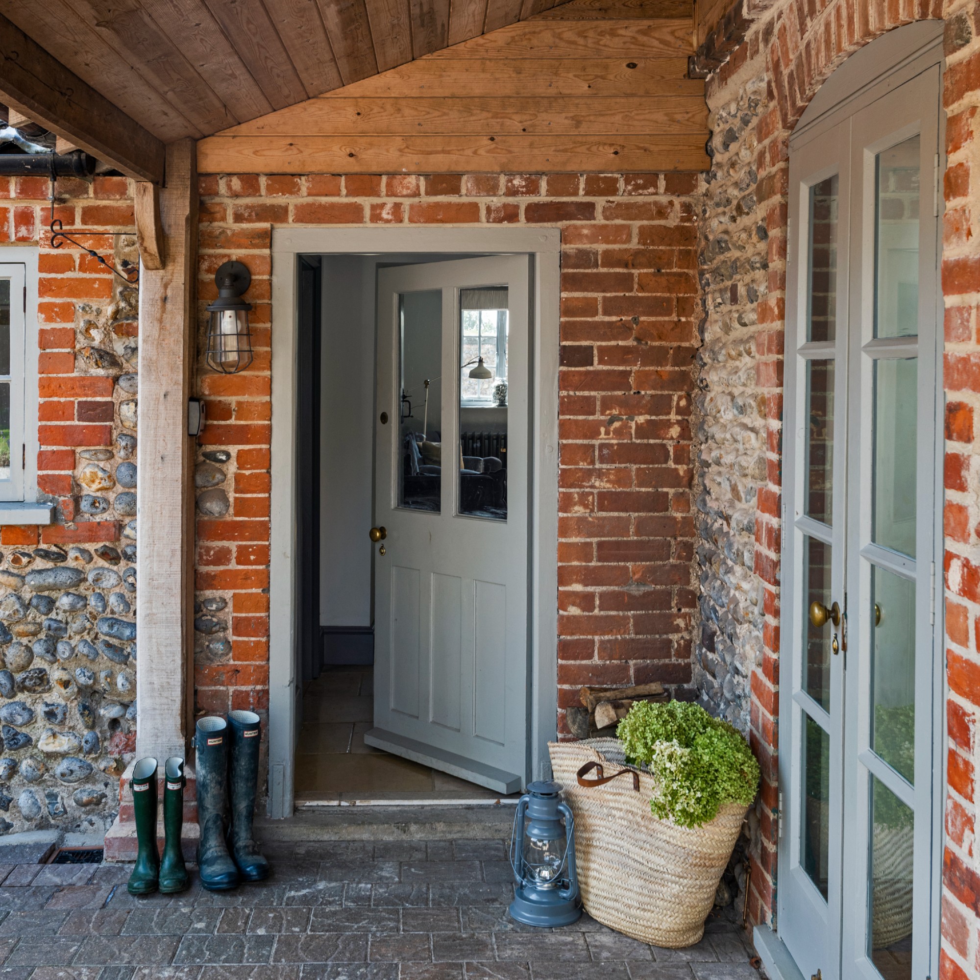A front porch with a grey front door with a wall light next to it and exposed red brick facade