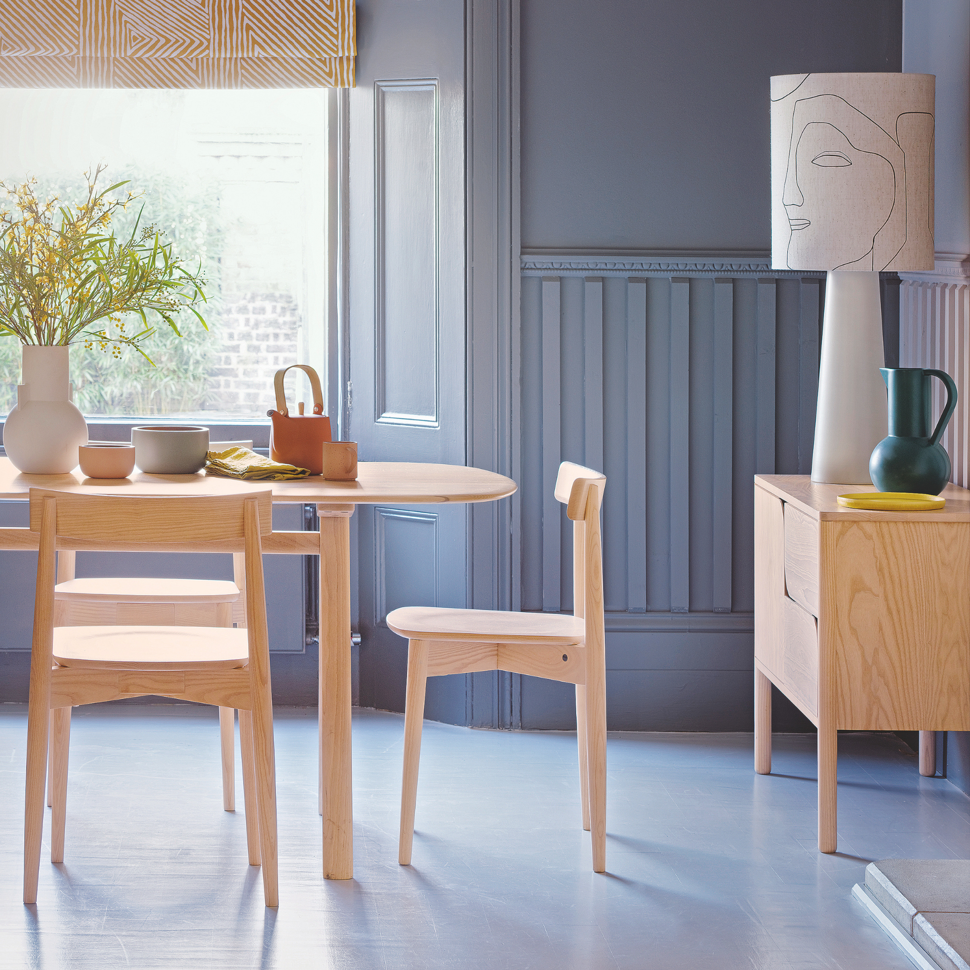 Dining room with blue flooring, blue wood panelling and shutters, wood table and chairs.